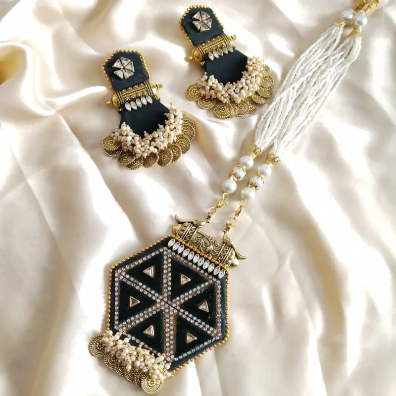 A handmade wedding necklace and earring set. It has a black hexagon pendant with a gold kundan pattern, pearls, and a white bead chain.