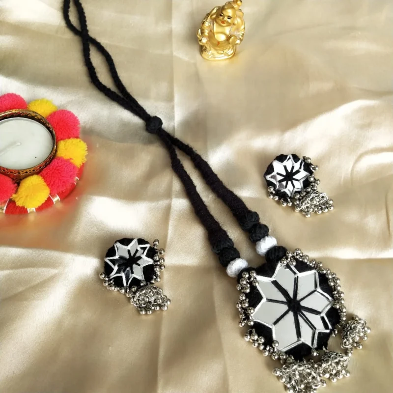 Handmade necklace and earring set with a large star-shaped mirror, black and white threadwork, and silver-toned jhumki charms on a black adjustable cord.