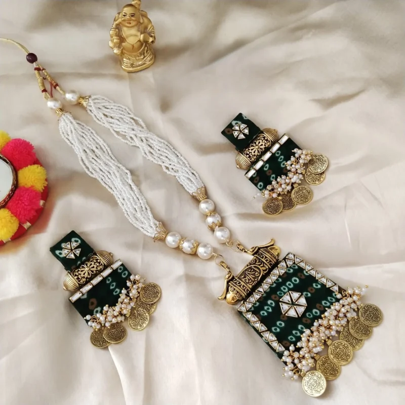 A handmade green bandhani fabric necklace and earring set. Features white pearl strands, antique gold coin charms, and kundan work on a cream cloth.