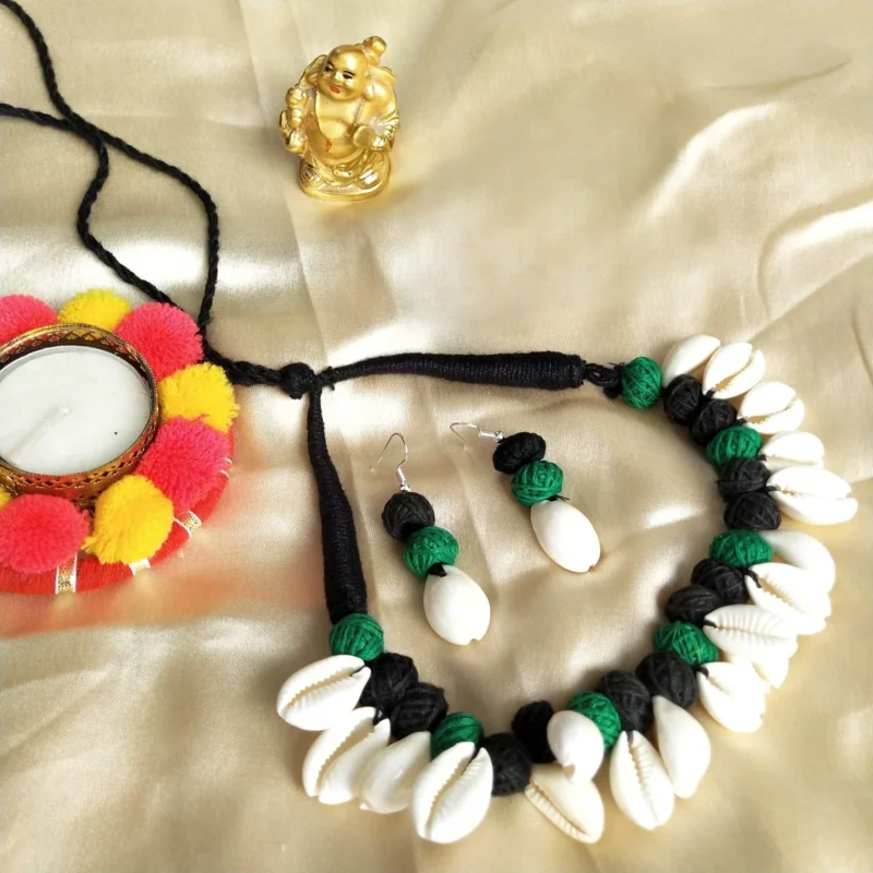 A handmade choker necklace and earrings with white cowrie shells and black and green thread beads on an adjustable black cord.