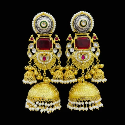 A pair of grand gold tone jhumka earrings with rectangular ruby red stones, preacock design, green enamel, and pearl detailing Black Background