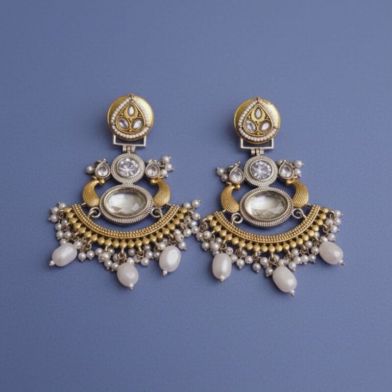 A pair of gold and silver Chandbali earrings with white pearls, a large translucent oval stone, and smaller white diamonds on a black background.