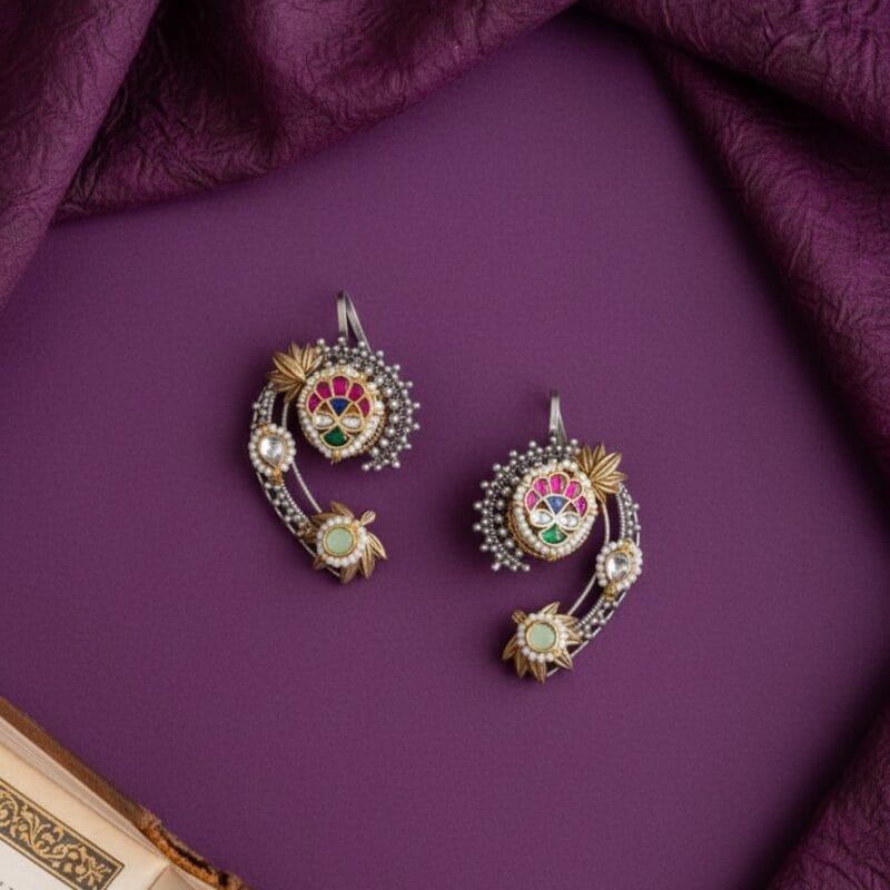 Pair of Kundan earcuffs with gold and silver details, colorful stones, and pearls displayed on a purple background.