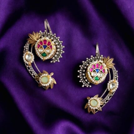Pair of Kundan earcuffs with gold and silver details, colorful stones, and pearls displayed on a dark purple silk cloth