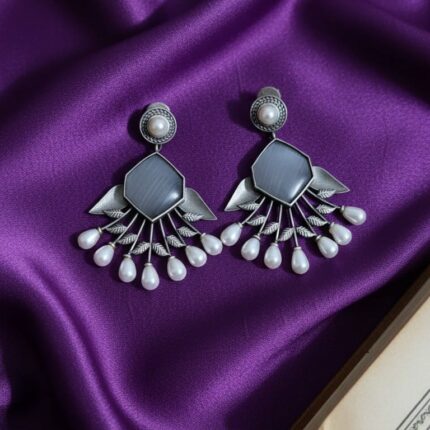 Pair of oxidized silver hexagon earrings with grey stone and white pearl drops on a purple silk cloth background.