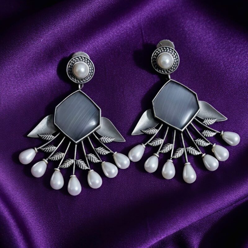 Pair of oxidized silver hexagon earrings with grey stone and white pearl drops on a purple silk cloth background.