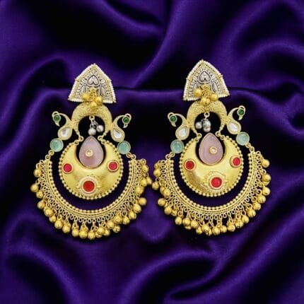 Pair of golden Chandbali earrings with red, green, and pink stones, delicate pearls, and dangling golden beads on a blue silk cloth