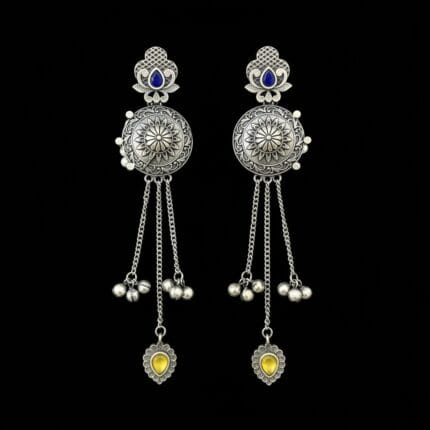 Pair of long traditional oxidized look tassel earrings with intricate patterns, blue stones at the top, and yellow heart-shaped stones at the bottom on black background