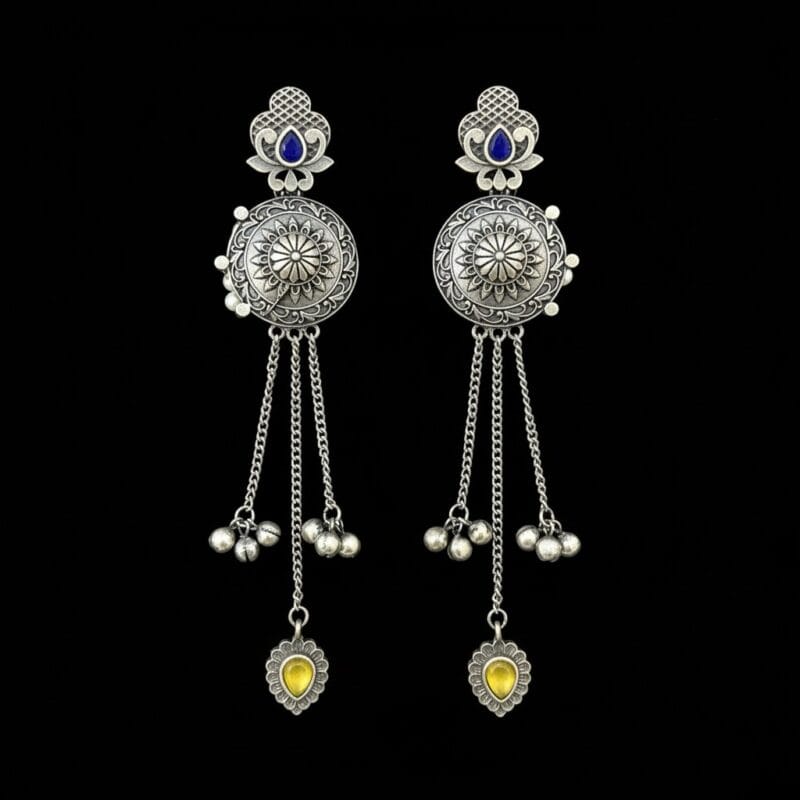 Pair of long traditional oxidized look tassel earrings with intricate patterns, blue stones at the top, and yellow heart-shaped stones at the bottom on black background