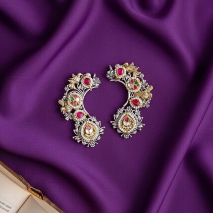 A pair of Royal Little Dove Kundan Earcuffs with silver, gold, red stones, green stones, and pearls, displayed on royal purple silk cloth