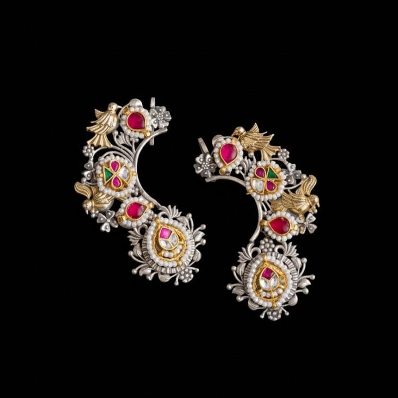 A pair of Royal Little Dove Kundan Earcuffs with silver, gold, red stones, green stones, and pearls, displayed on a black background