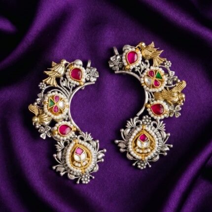 A pair of Royal Little Dove Kundan Earcuffs with silver, gold, red stones, green stones, and pearls, displayed on a bluish purple silk cloth