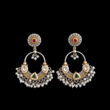 A pair of traditional silver and gold Chandbali earrings with red and green stones and hanging white pearls on a black background.