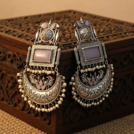 Close up of Swadeshi Oxidized Chandini Earrings with a lavender rectangular stone, crescent moon design, and pearl drops, on a carved wooden box.