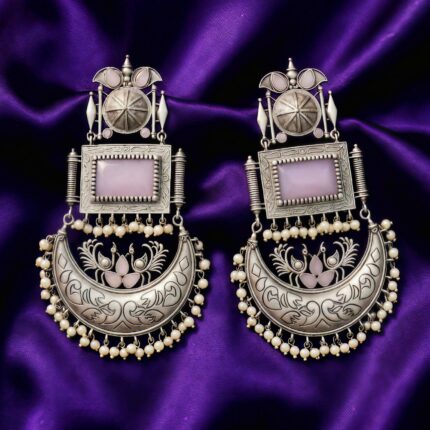 Close up of Swadeshi Oxidized Chandini Earrings with a lavender rectangular stone, crescent moon design, and pearl drops, on a purple silk cloth