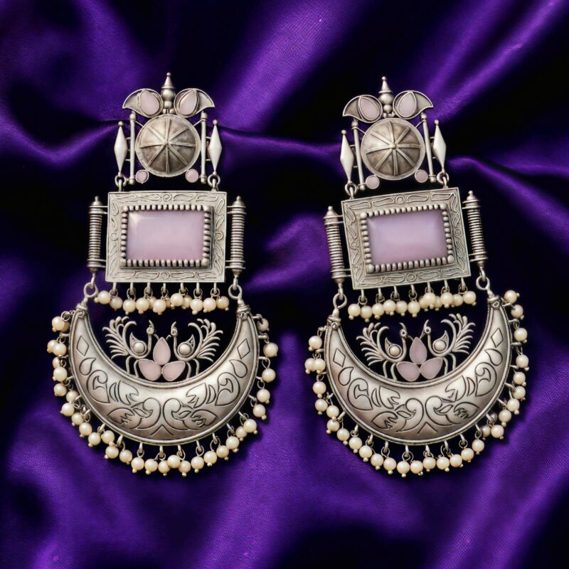 Close up of Swadeshi Oxidized Chandini Earrings with a lavender rectangular stone, crescent moon design, and pearl drops, on a purple silk cloth