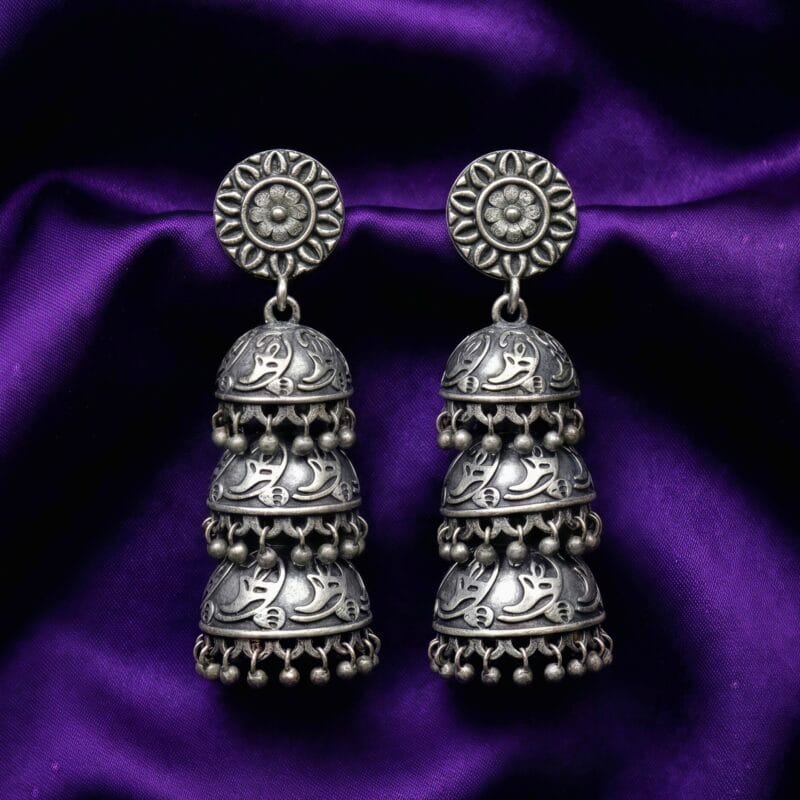 Three Tier Oxidized Jhumka Earrings placed on blueish purple silk cloth