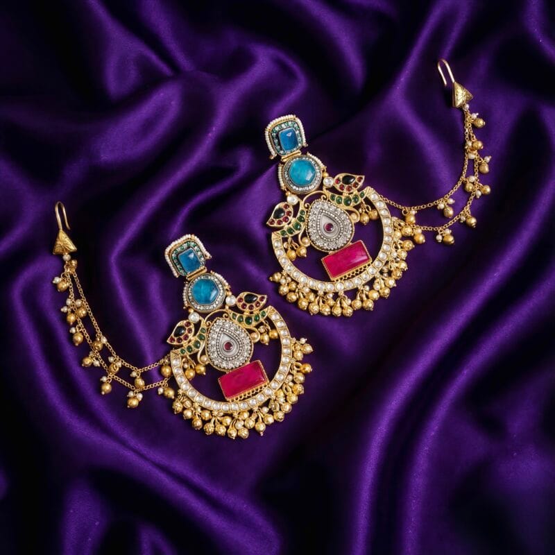Gold-tone chandbali earrings with pink and blue stones and triple-strand side chains on purple silk fabric