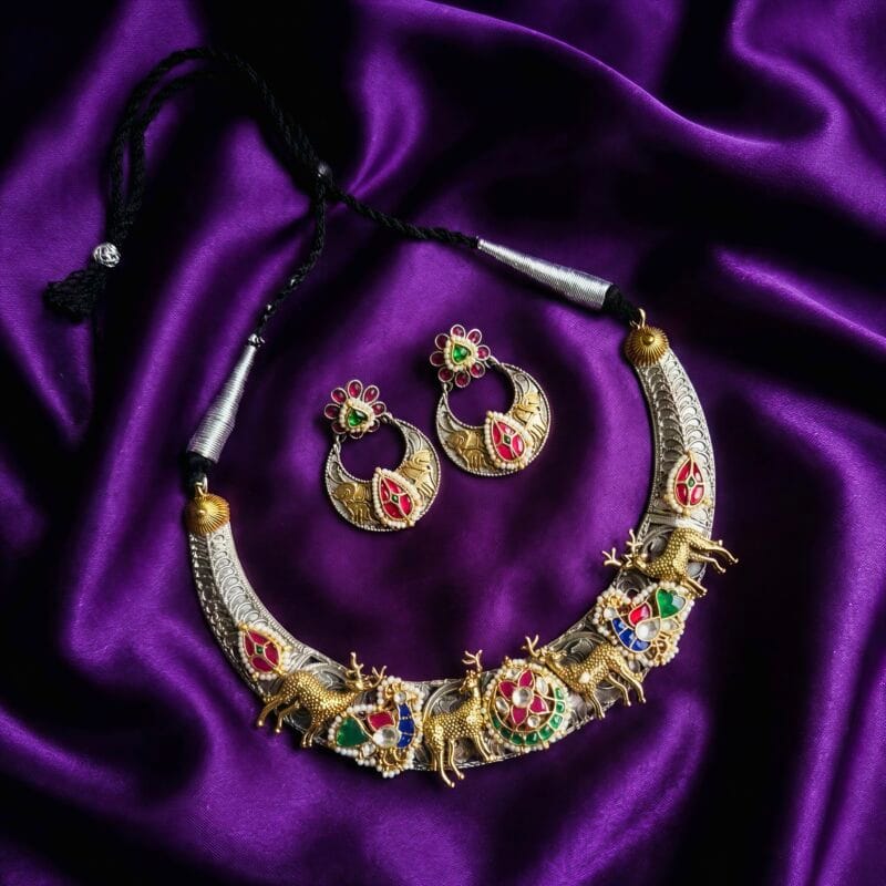 Traditional Indian choker necklace and earrings set with deer motifs, colorful red green blue stones, and white pearls on a purple silk background
