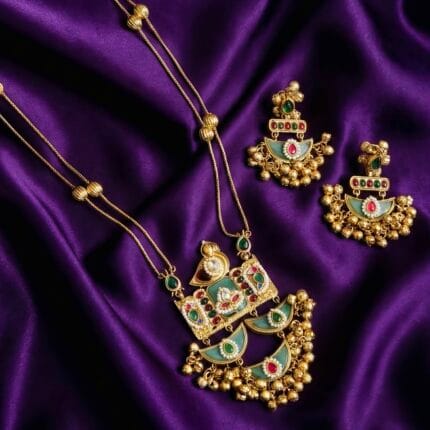 Long golden necklace with green stone crescent (chandbali) pendants and matching earrings on purple satin fabric
