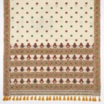 Closeup of off white bamboo cotton saree with green and maroon patterns and yellow tassels.