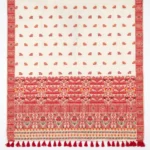 Assamese cream coloured saree with woven floral designs in red and yellow with large red tassels on border.