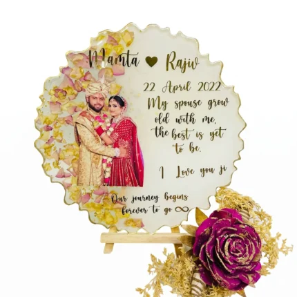 Round resin plaque with wedding photo, pink and yellow dry petals, gold foil and gold letters on a wooden stand.