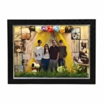 Deluxe 3D shadow box frame in black with a family scene, lit-up family photo cutouts, yellow fabric drapes and small Snoopy collectible figure on grass.
