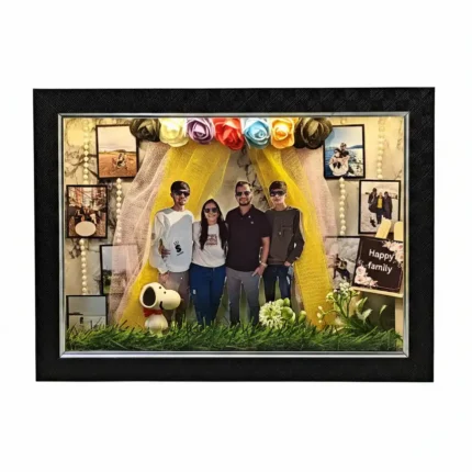 Deluxe 3D shadow box frame in black with a family scene, lit-up family photo cutouts, yellow fabric drapes and small Snoopy collectible figure on grass.