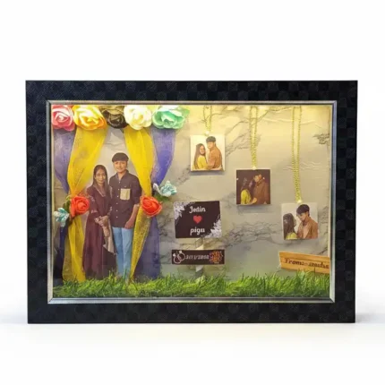 A textured black 3D shadow box frame with a couple photo cutout under fabric curtains, custom nameplates and 3 photos hanging from gold chains.